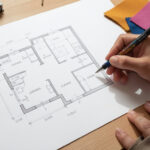 A designer sketching a floor plan alongside fabric swatches]