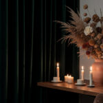 A moody study corner with velvet curtains, candles, and a dried botanical arrangement on a wooden shelf.