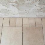 A tile floor in progress showing the centered chalk line layout method, with a dry-laid row of tiles extending from the center to the wall before any adhesive is applied.