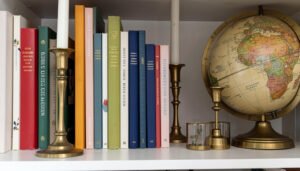 Close-up of styled bookshelf with color-coordinated books, brass candleholders, and vintage globe