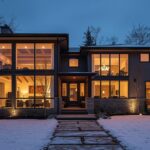 Modern home exterior with large triple-pane energy-efficient windows, showing frost-free glass in winter with warm interior lighting