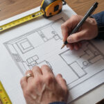 Person sketching a room layout on graph paper with a tape measure nearby