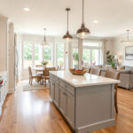 A bright open-concept kitchen flowing into a dining and living area, with a large island acting as the visual anchor between the spaces.