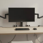 A minimalist desk setup with hidden cable management, wireless charging pad, and dual monitor arms in a neutral-toned office.