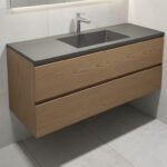 A modern floating vanity with a matte oak finish and integrated sink, mounted above light gray floor tiles in a compact bathroom.