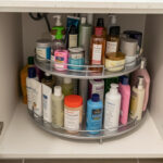 A rotating lazy Susan organizer inside an under-sink bathroom cabinet filled with skincare and cleaning bottles.