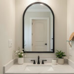 Arched black-framed mirror above a bathroom sink
