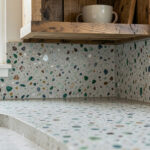 Close-up of a sustainable kitchen countertop made from recycled glass and concrete, paired with reclaimed wood open shelving.